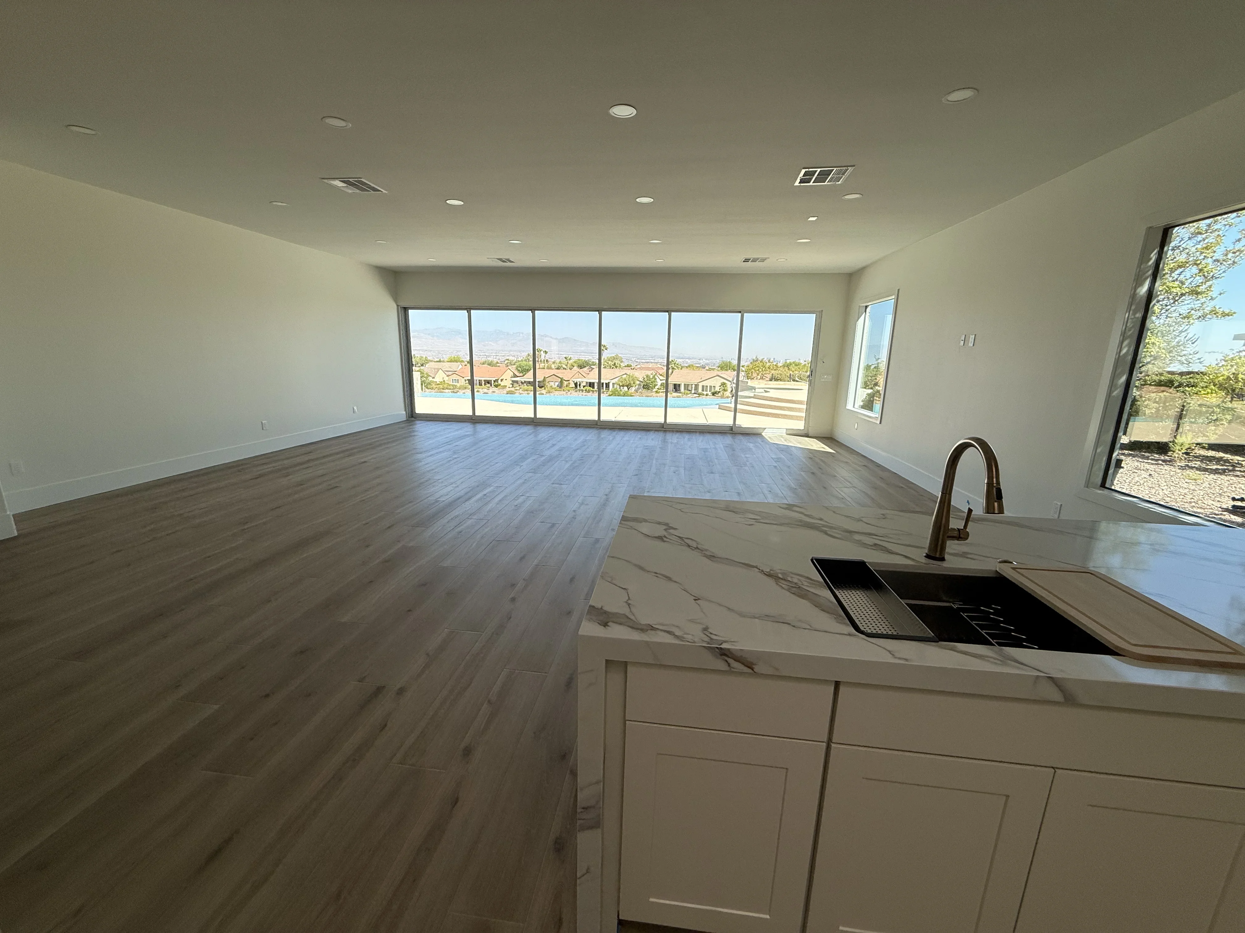 Open kitchen and living room with hardwood floors, marble island, and multi-panel glass doors overlooking water