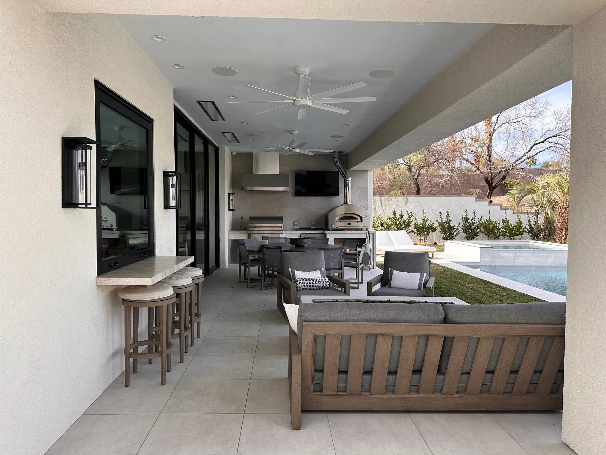 Covered patio with outdoor kitchen, pizza oven, dining area, and pool view