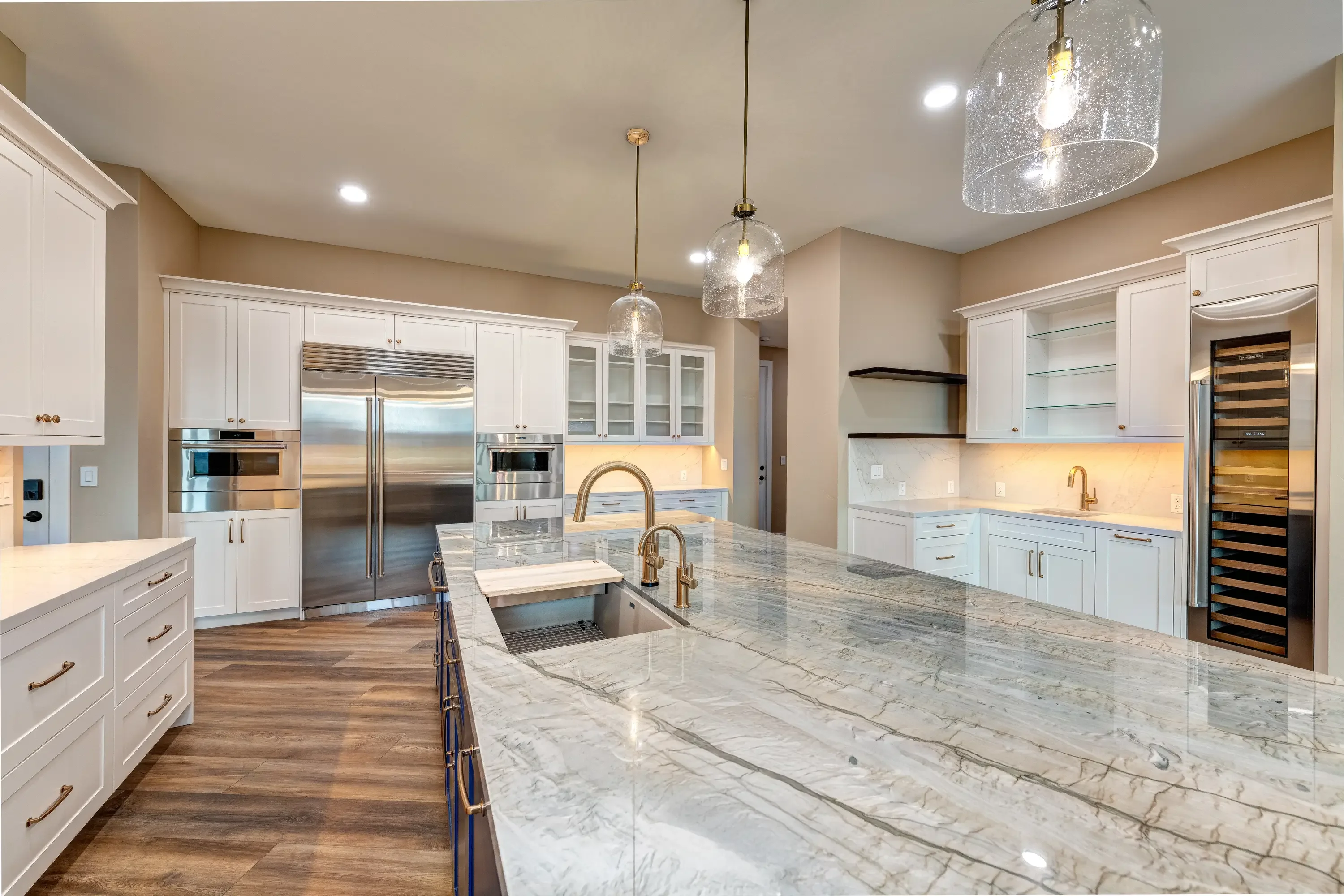 White kitchen cabinets, marble countertops, stainless steel appliances, brass fixtures, wood flooring