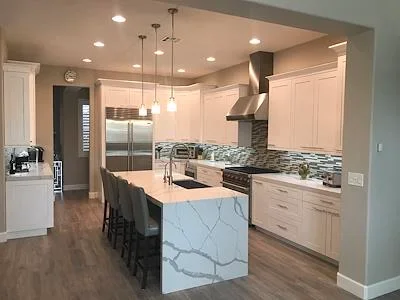 Modern kitchen with white cabinets, marble waterfall island, stainless appliances, and pendant lighting