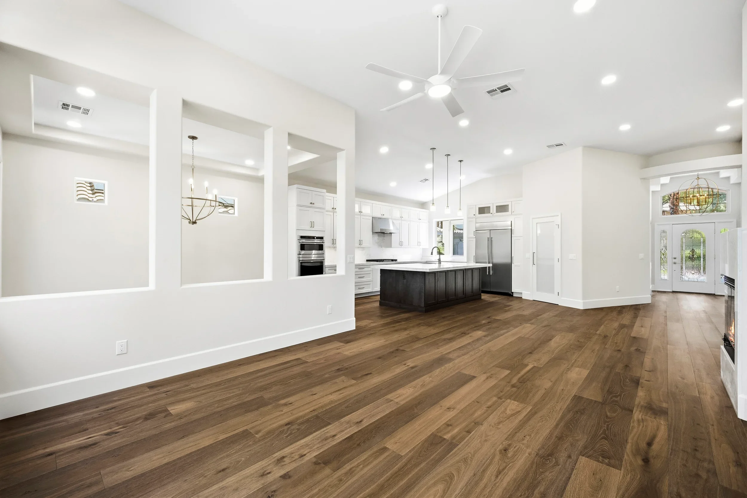 Open concept kitchen with white cabinets, black island, hardwood floors, and modern lighting fixtures