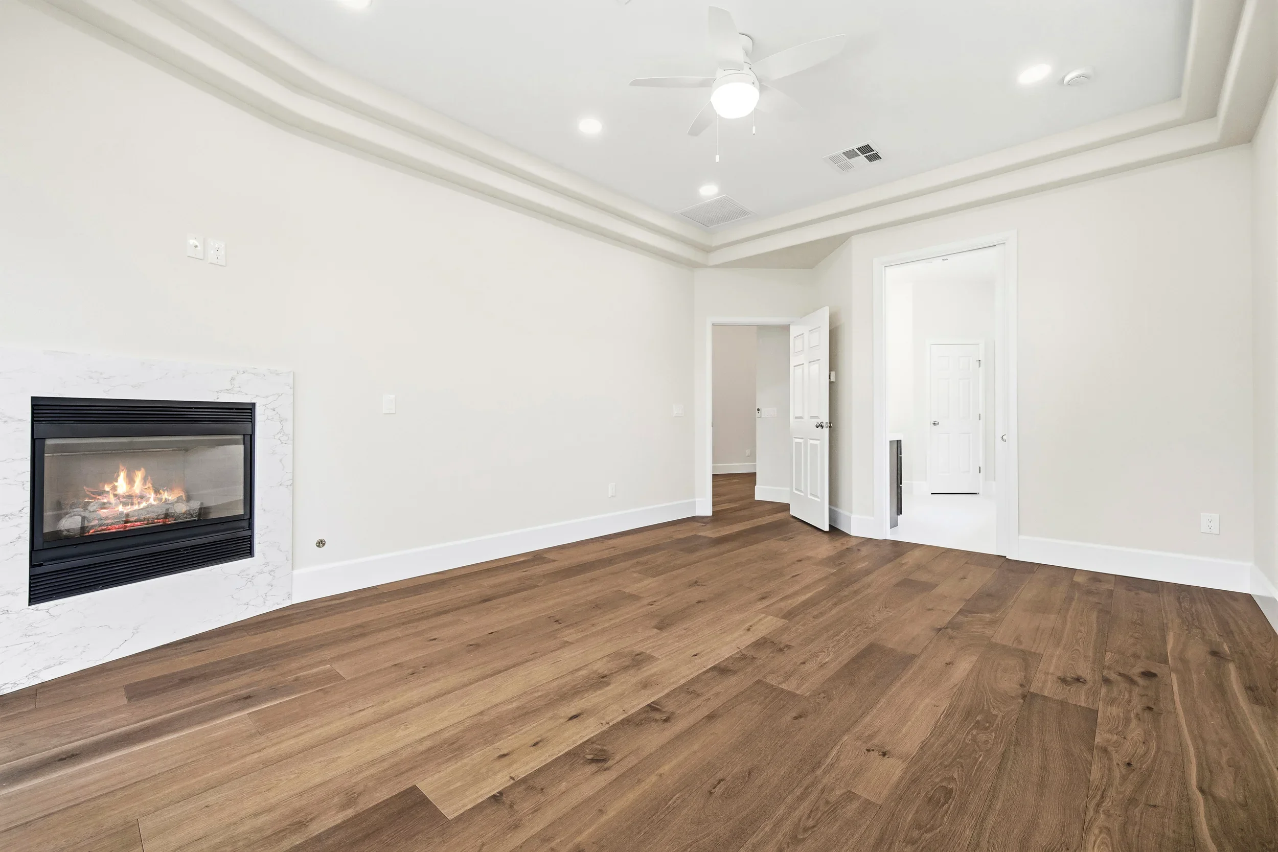Master bedroom with marble fireplace, hardwood floors, coffered ceiling, and white trim