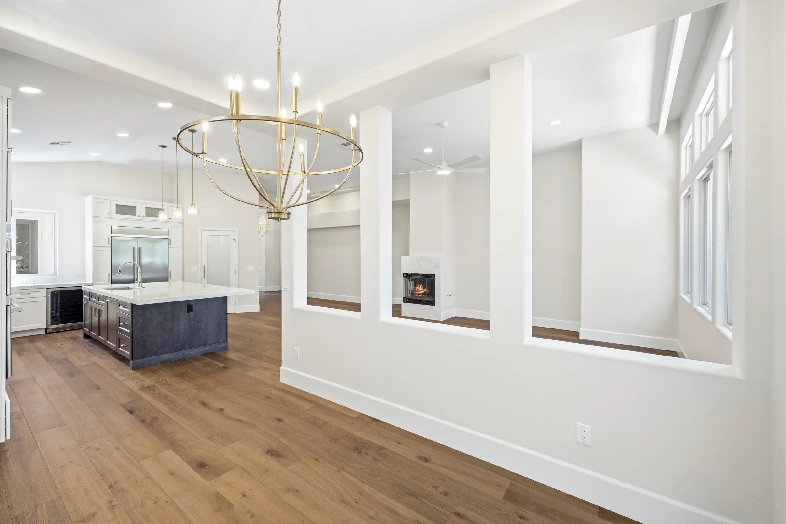 Open concept kitchen with dark island, white cabinetry, hardwood floors, and brass pendant lighting