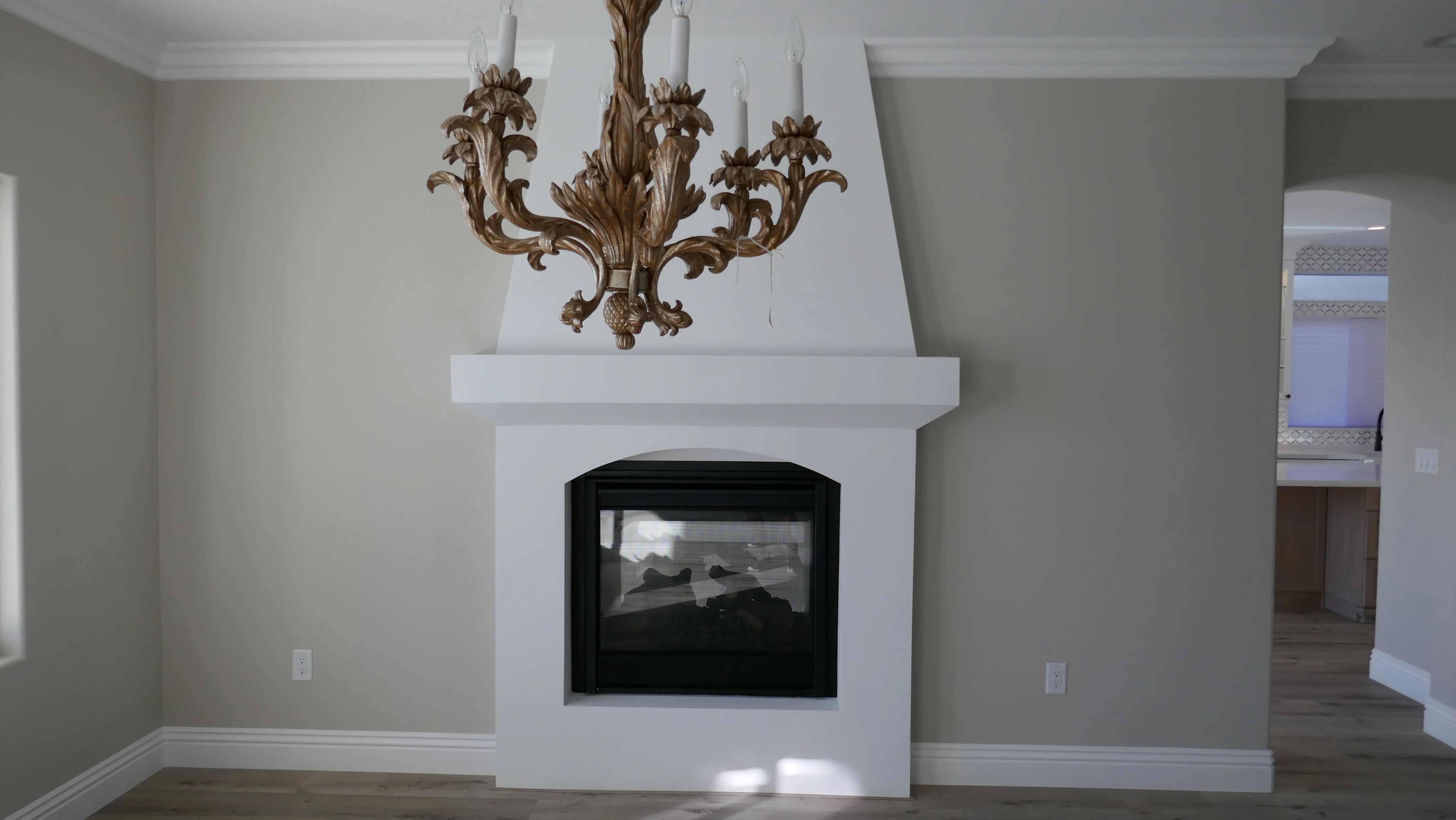 White drywall fireplace surround with black gas insert and decorative gold chandelier above mantel